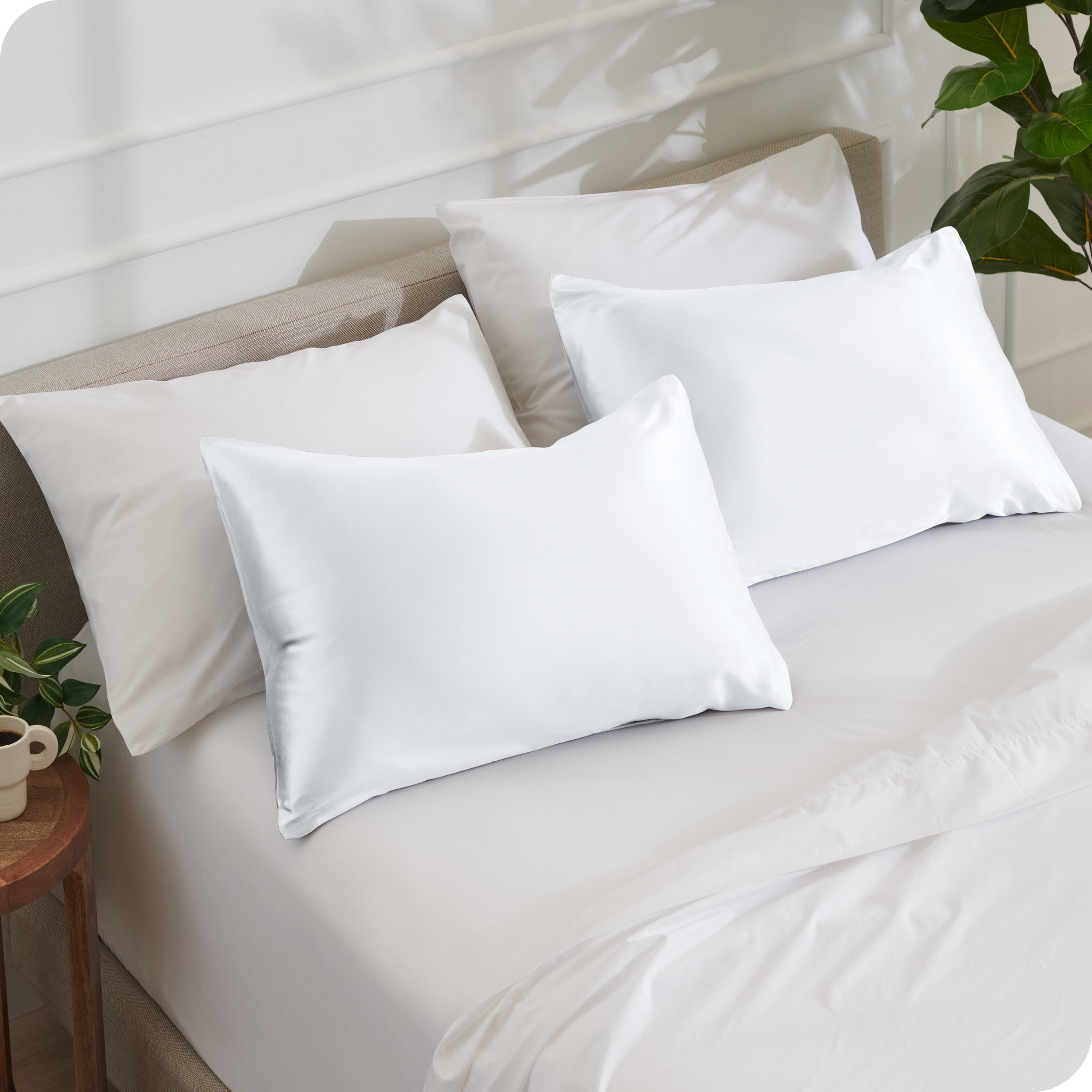 2 satin pillowcases on pillows leaning against other pillows on a bed