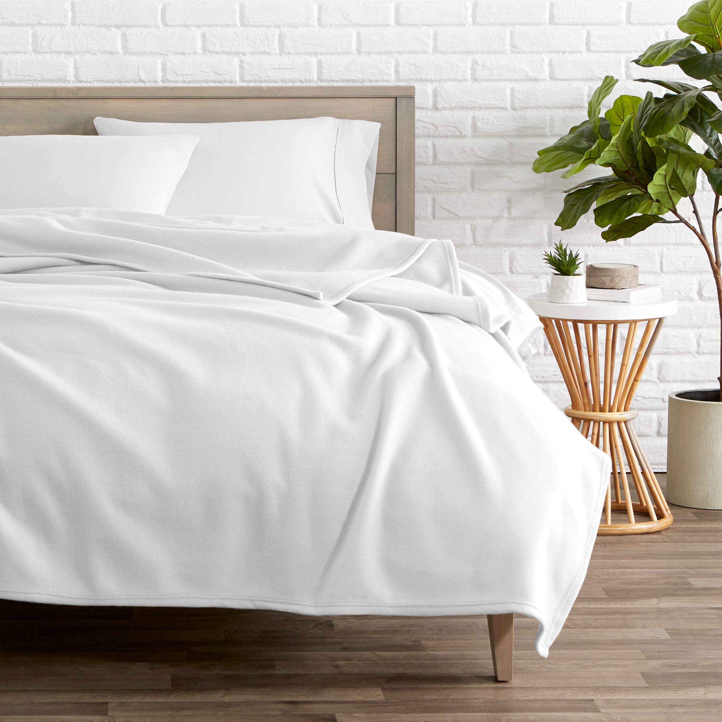 A polar fleece blanket on a bed next to a table and a large plant