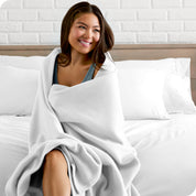 A woman sitting at the end of a bed with a fleece blanket wrapped around her shoulders