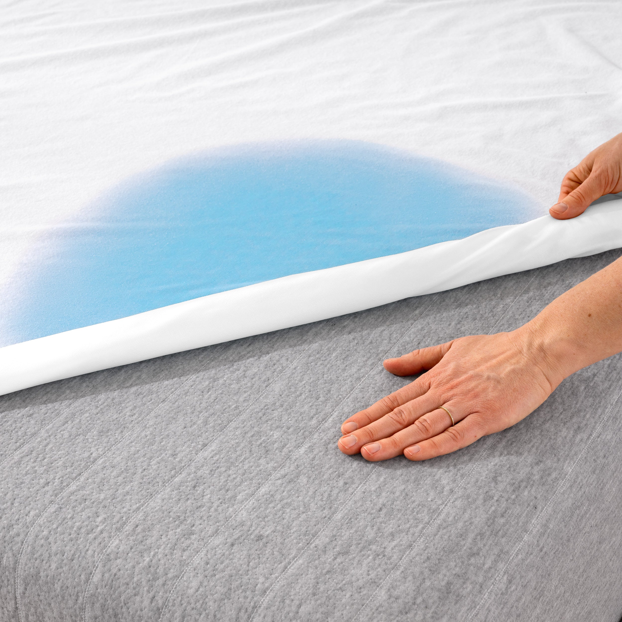 A hand is feeling the dry mattress underneath the wet mattress protector.