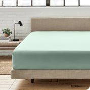 A percale fitted sheet on a bed with table next to it