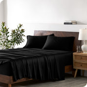 Modern bedroom with a bed against a white wall with a nightstand next to the bed. The bed has bamboo sheets draped over it.