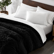 Diagonal view of a bed made with white sheets and pillowcases with a black shaggy duvet cover on top