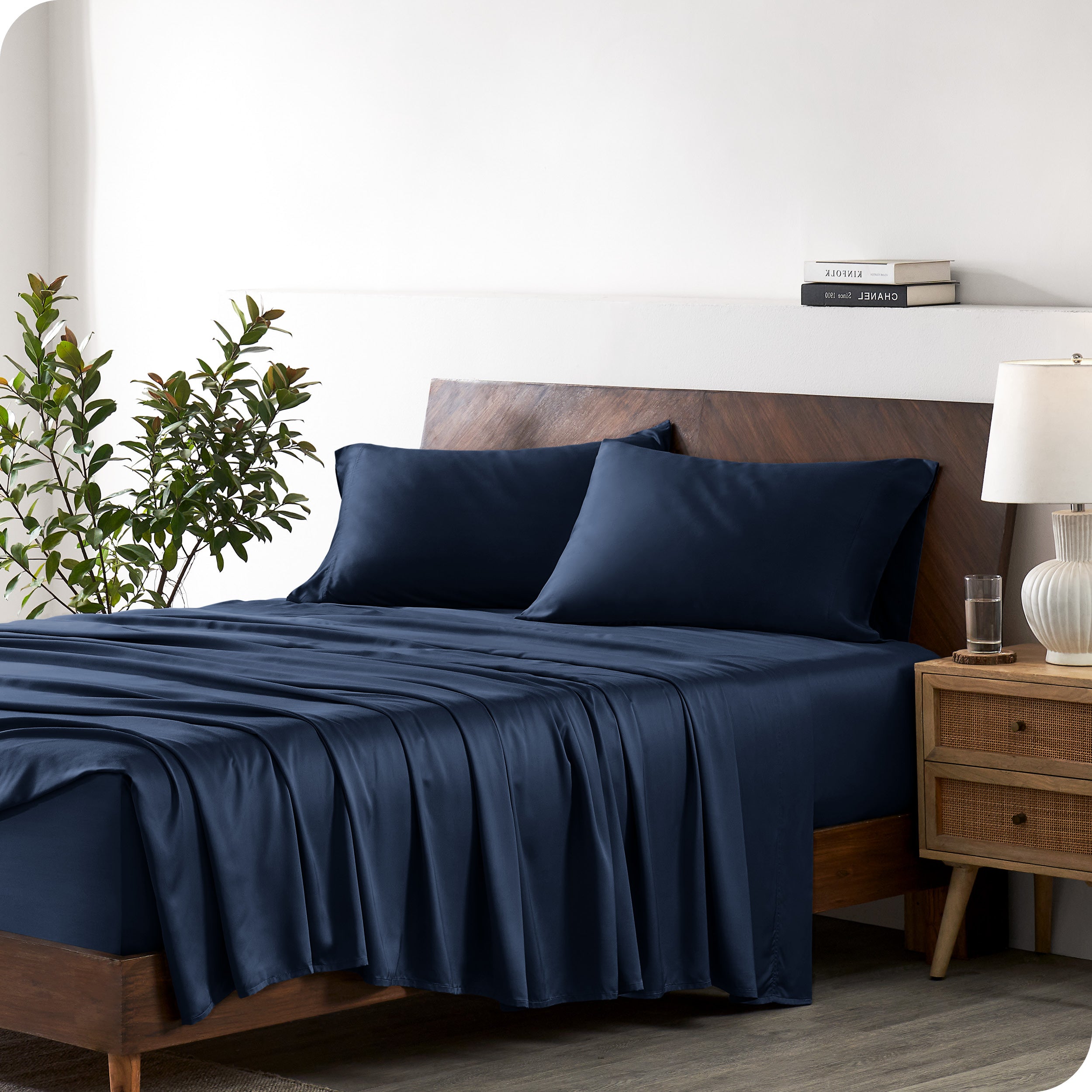 Modern bedroom with a bed against a white wall with a nightstand next to the bed. The bed has bamboo sheets draped over it.