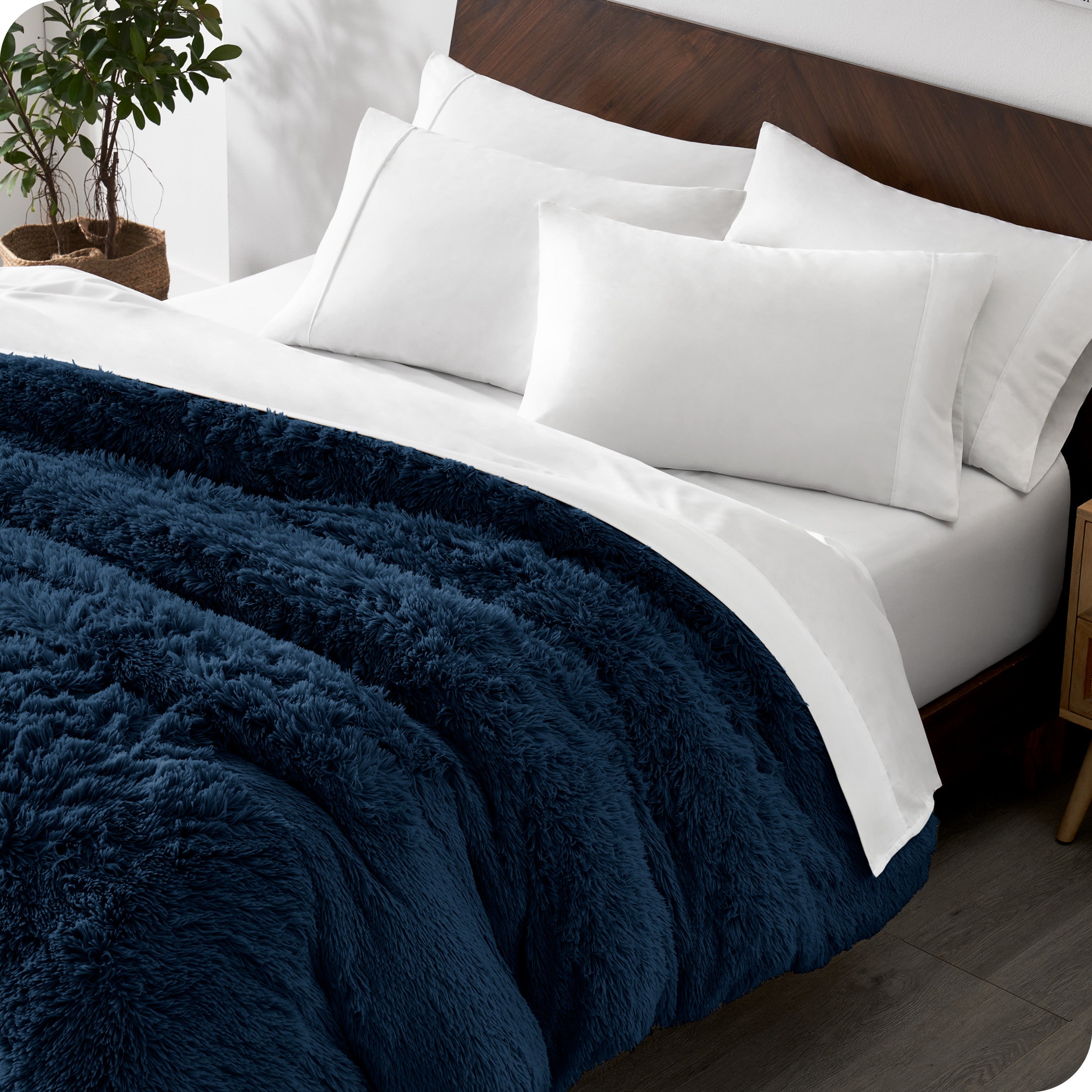 Diagonal view of a bed made with white sheets and pillowcases with a dark blue shaggy duvet cover on top