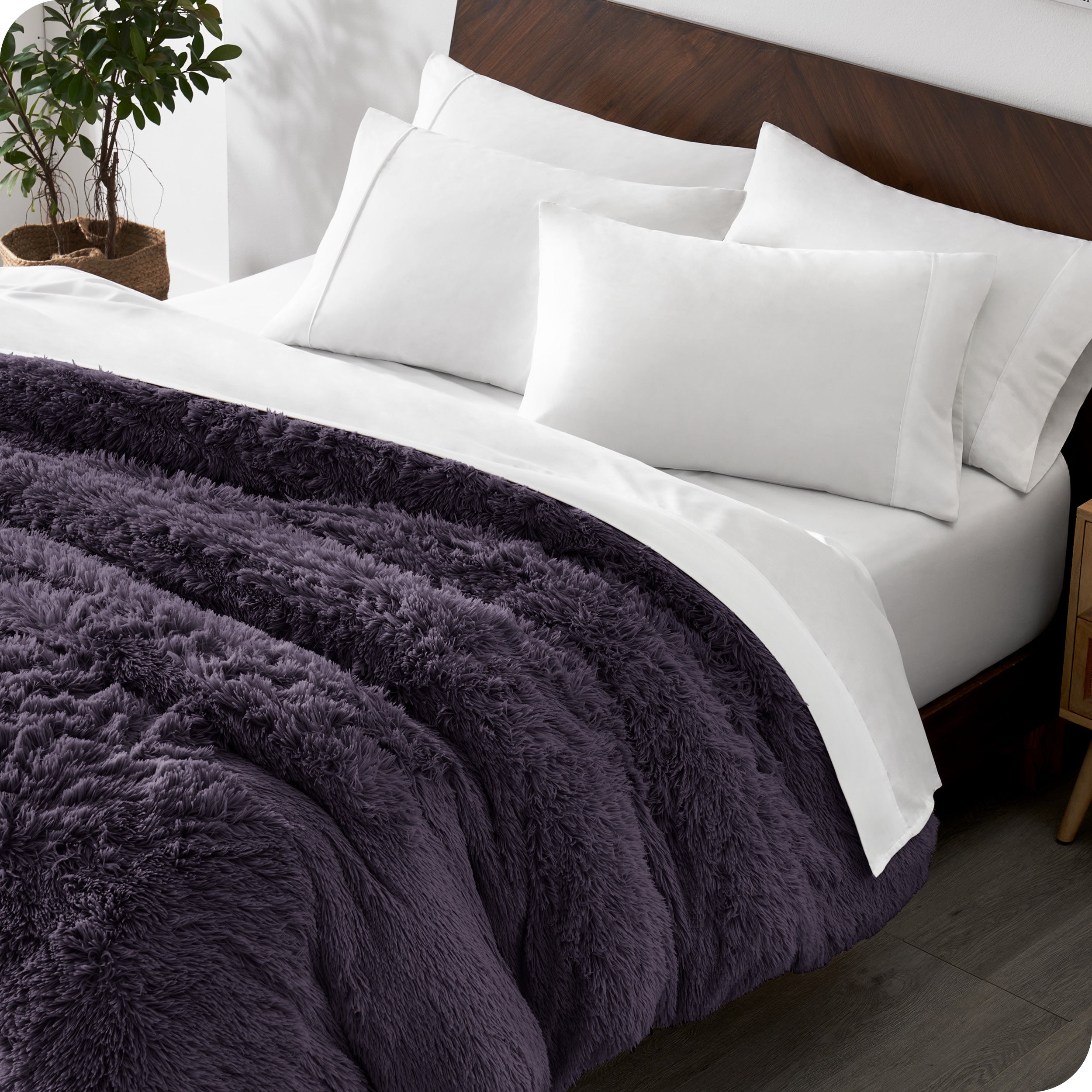 Diagonal view of a bed made with white sheets and pillowcases with a purple shaggy duvet cover on top