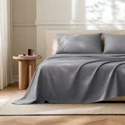 Gray flat sheet with matched pillowcases on a bed in a bedroom with a wooden side table.