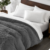 Diagonal view of a bed made with white sheets and pillowcases with a grey shaggy duvet cover on top