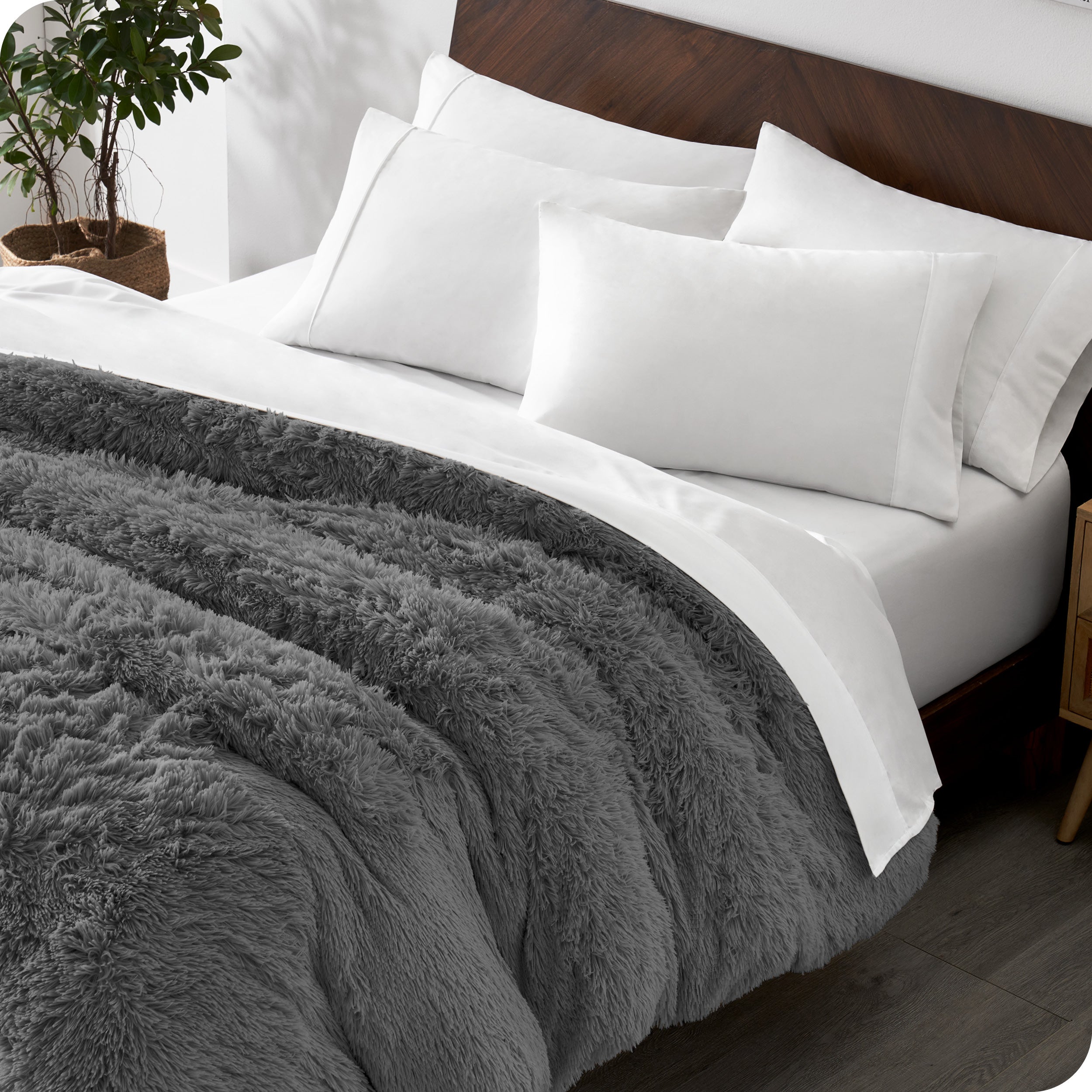 Diagonal view of a bed made with white sheets and pillowcases with a grey shaggy duvet cover on top