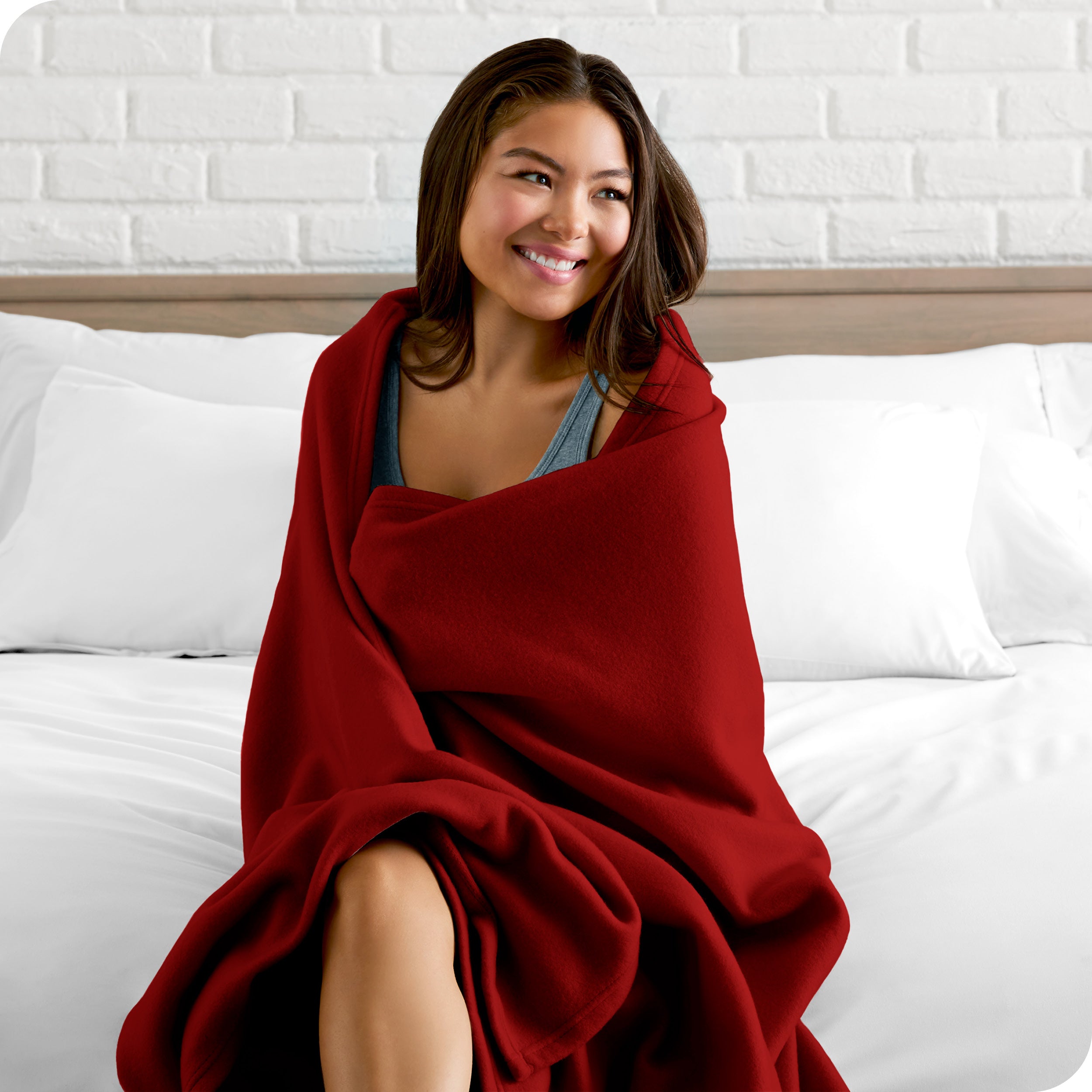 A woman sitting at the end of a bed with a fleece blanket wrapped around her shoulders