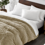 Diagonal view of a bed made with white sheets and pillowcases with a sand shaggy duvet cover on top