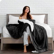 Woman cuddling with a sherpa blanket while sitting on the end of a bed