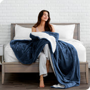 Woman cuddling with a sherpa blanket while sitting on the end of a bed