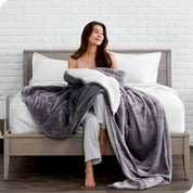 Woman cuddling with a sherpa blanket while sitting on the end of a bed