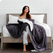 Woman cuddling with a sherpa blanket while sitting on the end of a bed