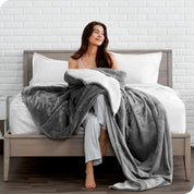 Woman cuddling with a sherpa blanket while sitting on the end of a bed