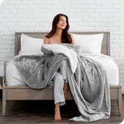 Woman cuddling with a sherpa blanket while sitting on the end of a bed