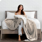 Woman cuddling with a sherpa blanket while sitting on the end of a bed