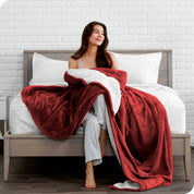 Woman cuddling with a sherpa blanket while sitting on the end of a bed