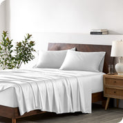 Modern bedroom with a bed against a white wall with a nightstand next to the bed. The bed has bamboo sheets draped over it.