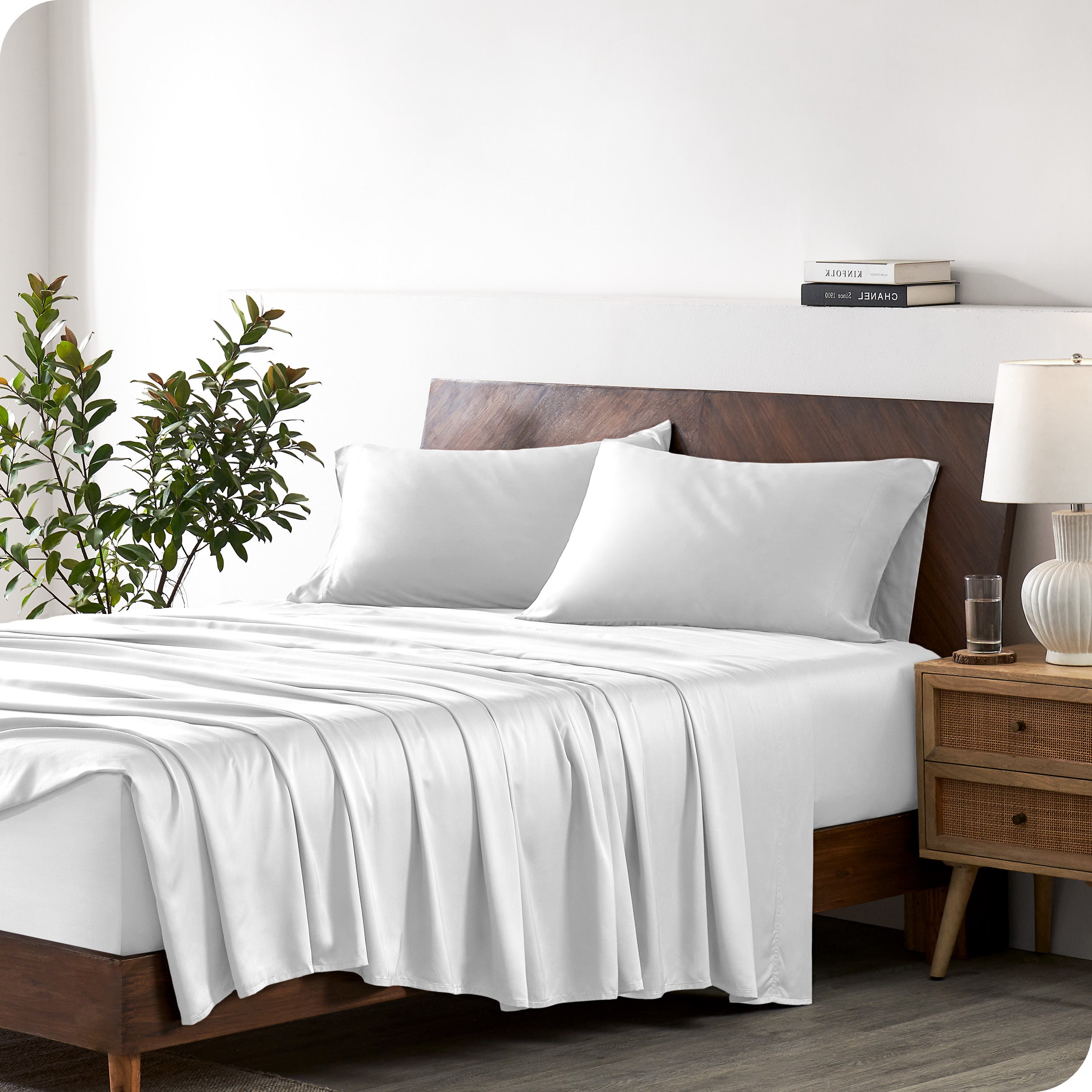 Modern bedroom with a bed against a white wall with a nightstand next to the bed. The bed has bamboo sheets draped over it.