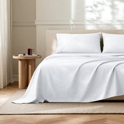 White flat sheet with matched pillowcases on a bed in a bedroom with a wooden side table.