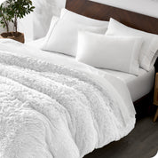 Diagonal view of a bed made with white sheets and pillowcases with a white shaggy duvet cover on top
