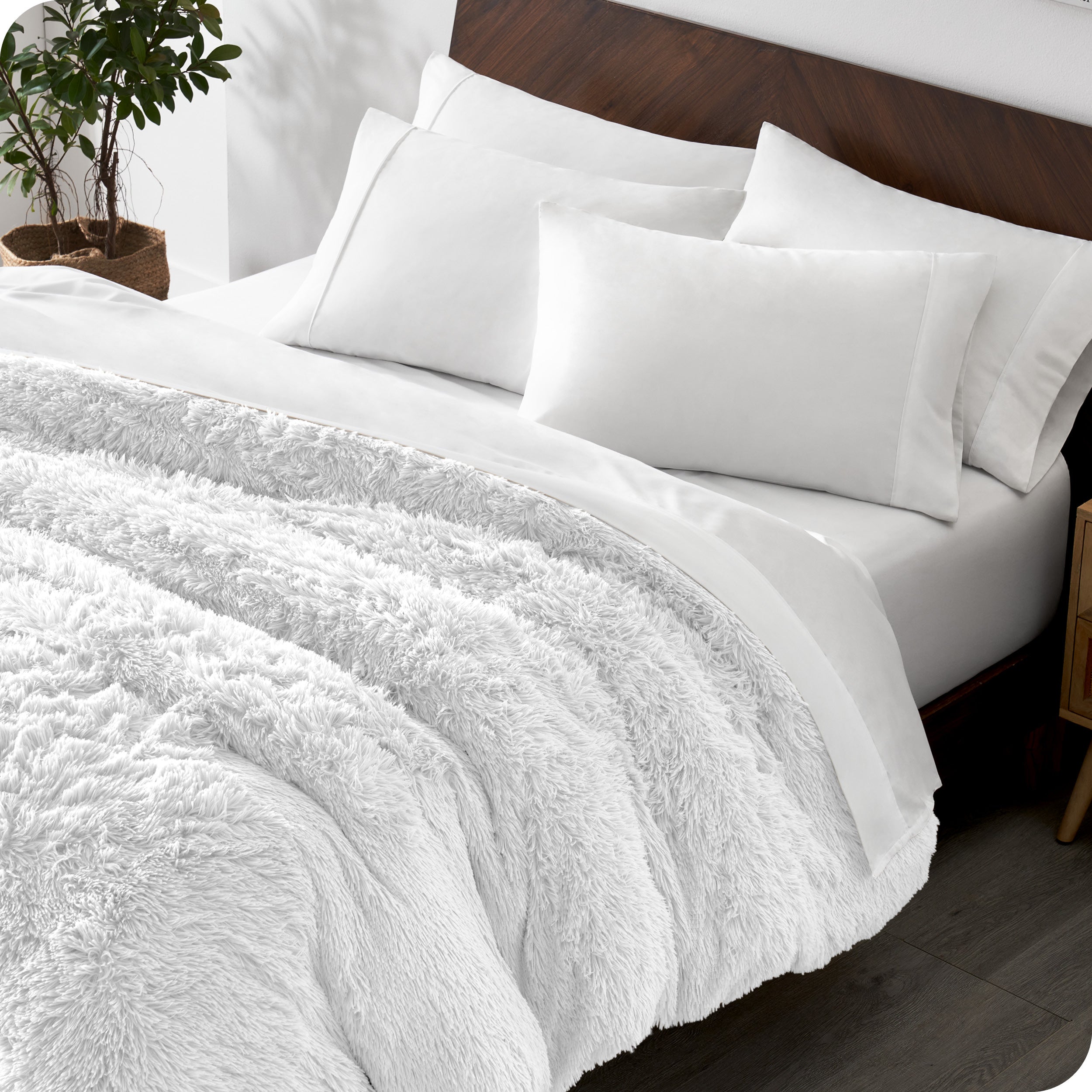 Diagonal view of a bed made with white sheets and pillowcases with a white shaggy duvet cover on top